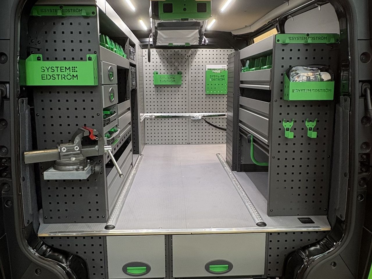 Innenraum eines ausgebauten Kia PV5 Cargo L2H1, von den Hecktüren aus gesehen: Metallregale an beiden Seitenwänden und Schubladenkasten unter der Bodenplatte